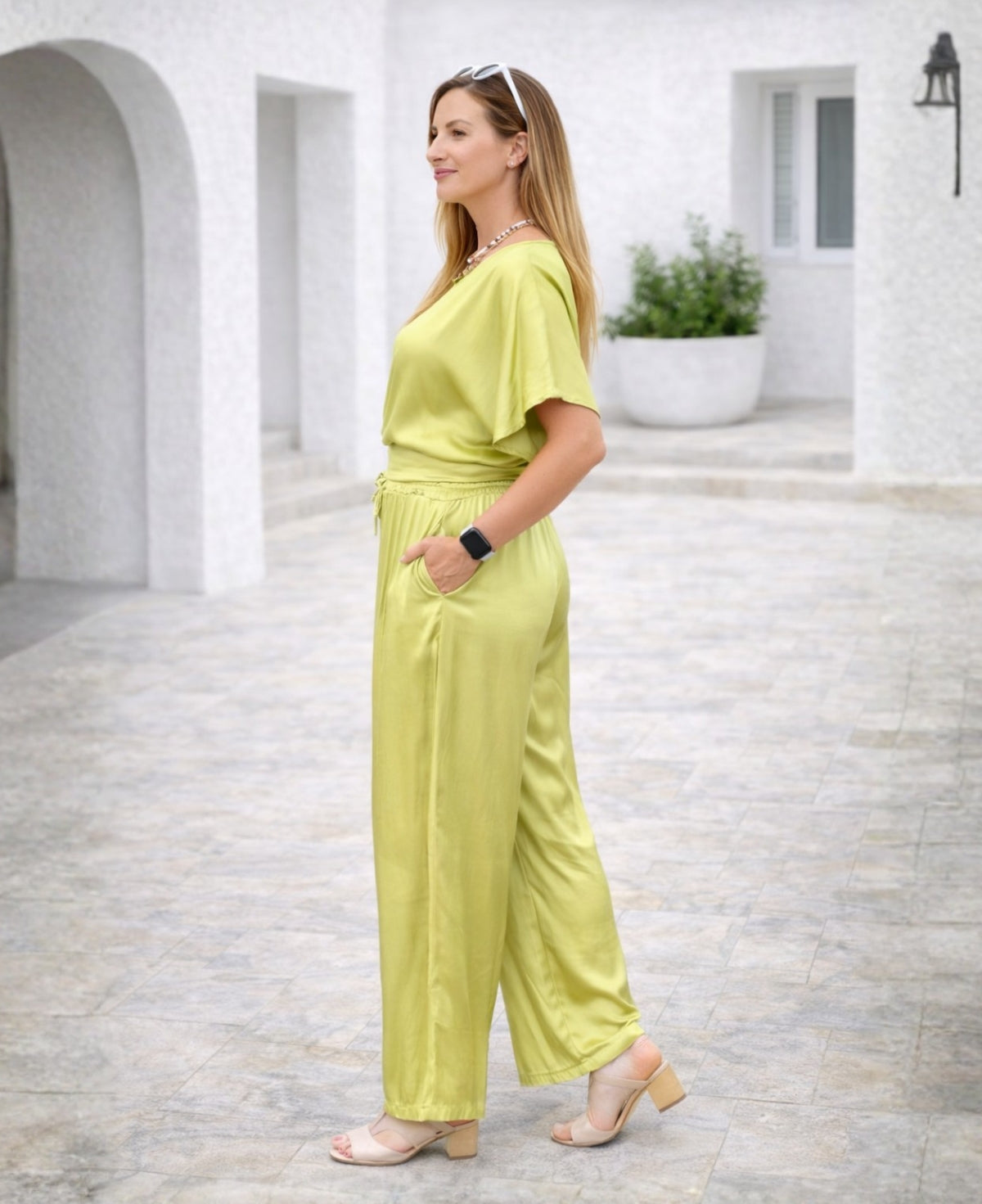 Side view of chartreuse Juliette satin pants showing fluid drape and elegant silhouette in a Mediterranean terrace location