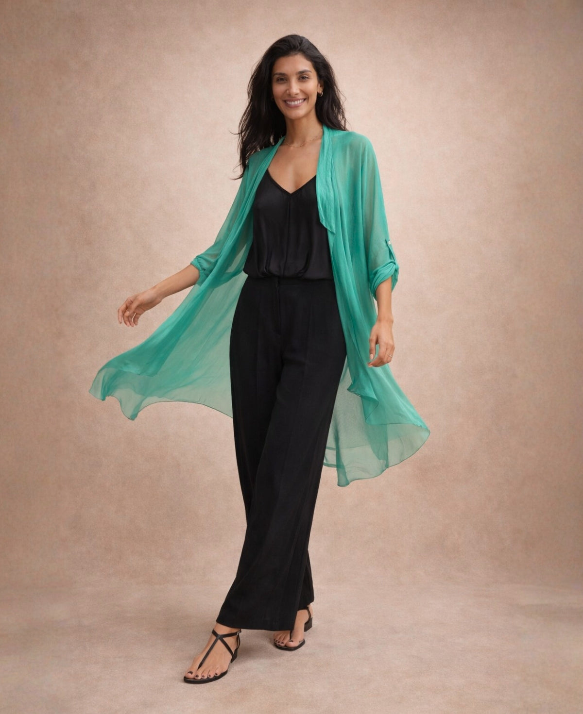 Katherine Sheer Silk Overlay in emerald green styled with black wide-leg trousers, captured in motion to showcase the flowing silk fabric and elegant drape.
