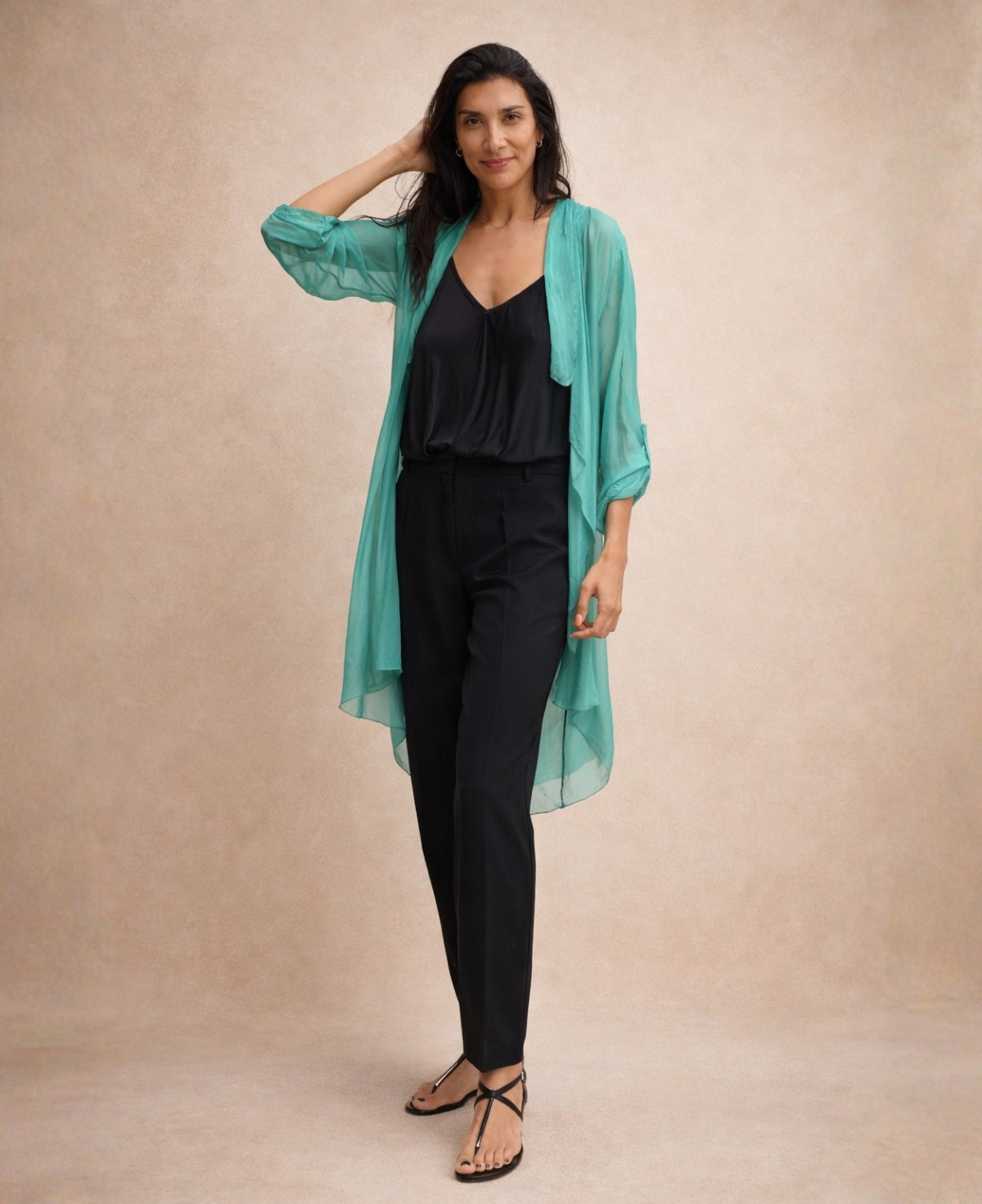 Model wearing the Katherine Sheer Silk Overlay in emerald green styled with a black camisole and tailored black trousers against a warm neutral studio background.