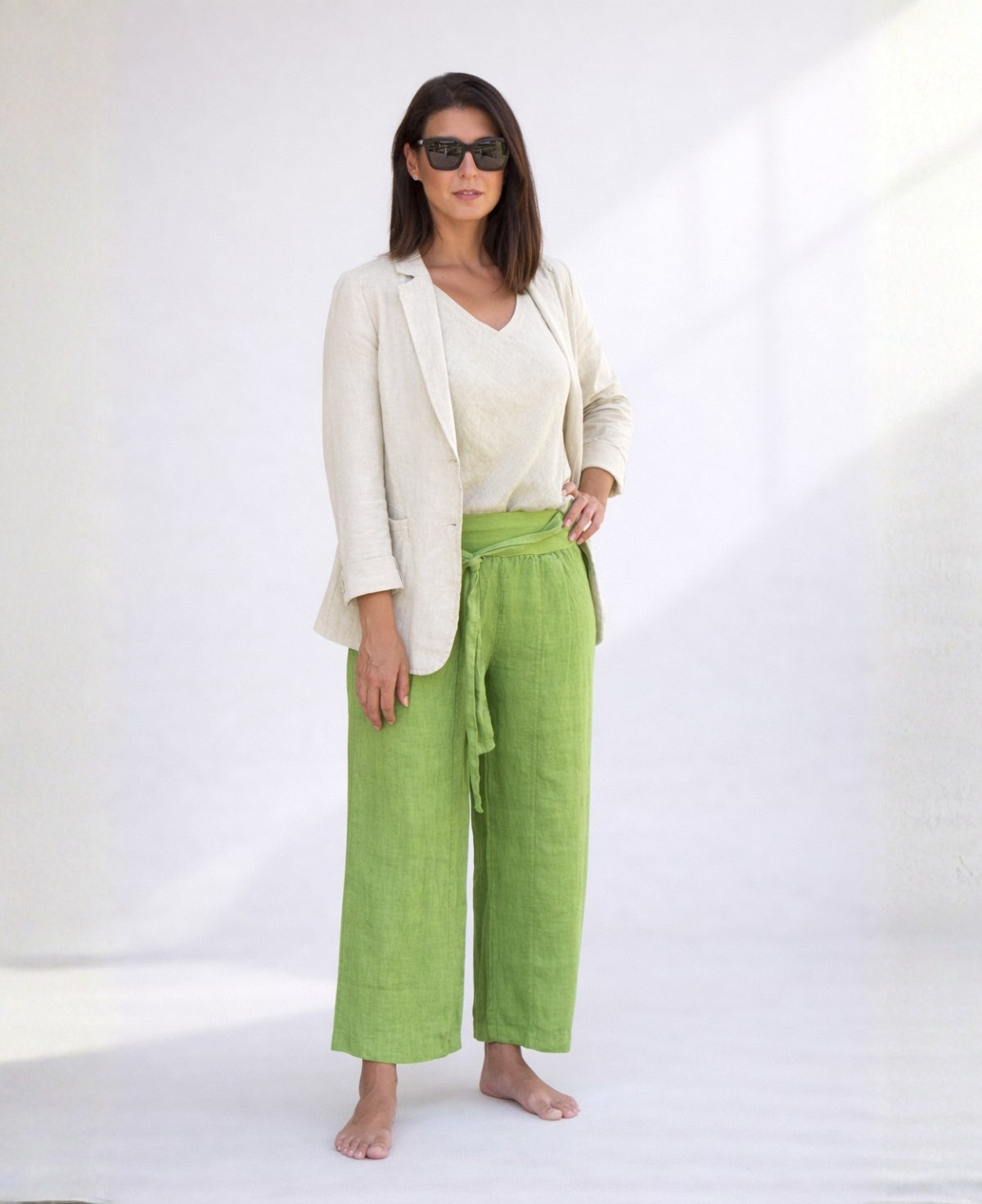 Woman wearing kiwi green linen palazzo pants styled with a linen blazer and sleeveless top, showing wide leg fit, stretch waist, and lightweight linen texture.