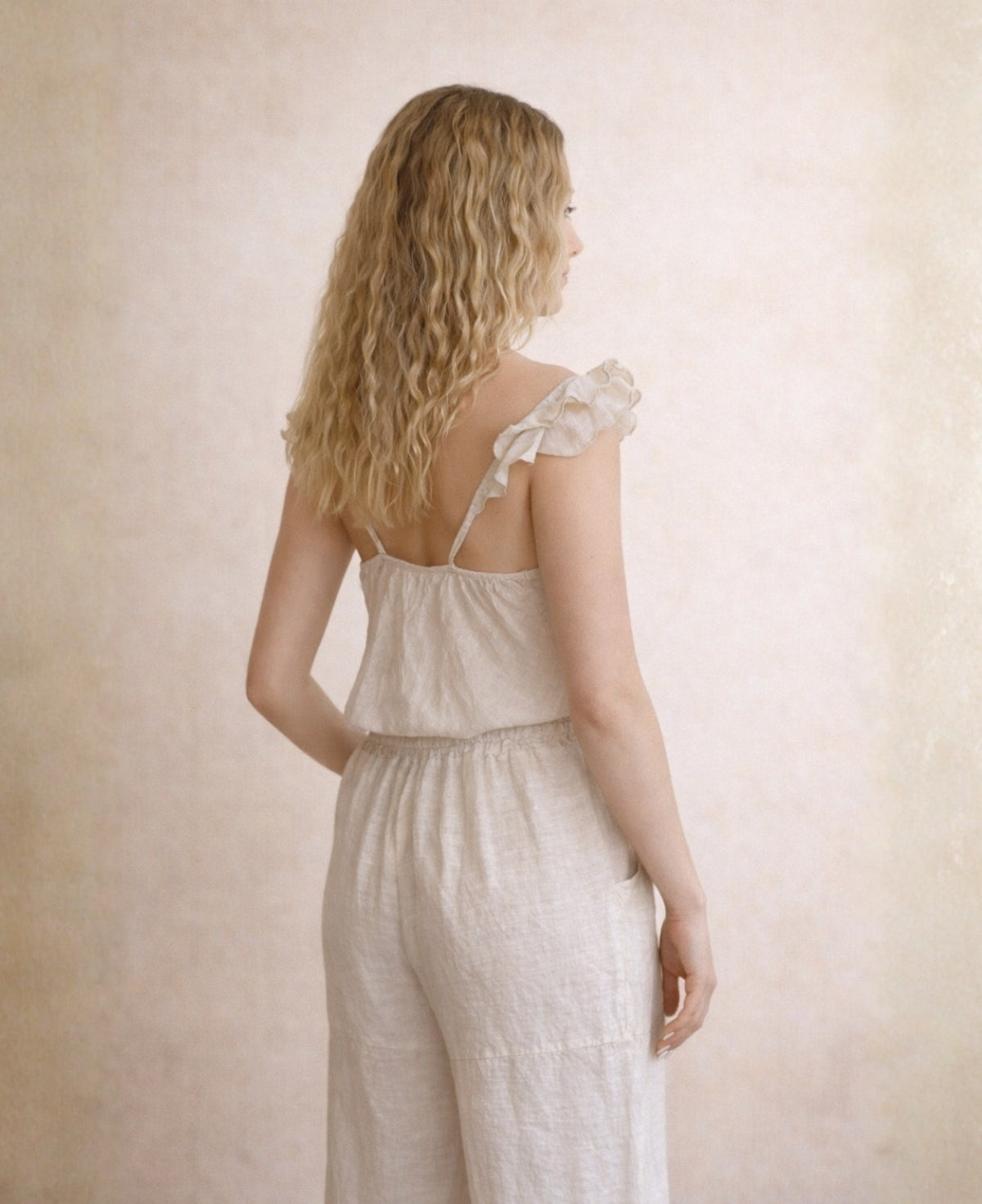 Back angled view of the Lydia Linen Top in oat styled with matching linen pants highlighting the soft ruffled straps and natural linen drape.