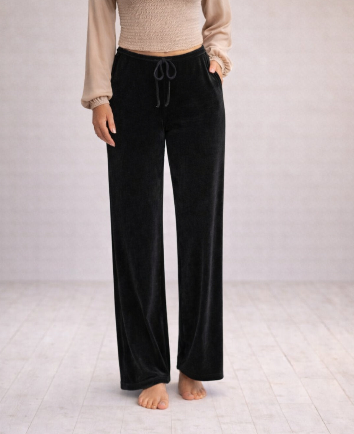 Close-up of black Marshmallow Lounge Pants showing the soft velour texture, relaxed wide-leg cut, and fluid drape, photographed in warm minimalist studio lighting.