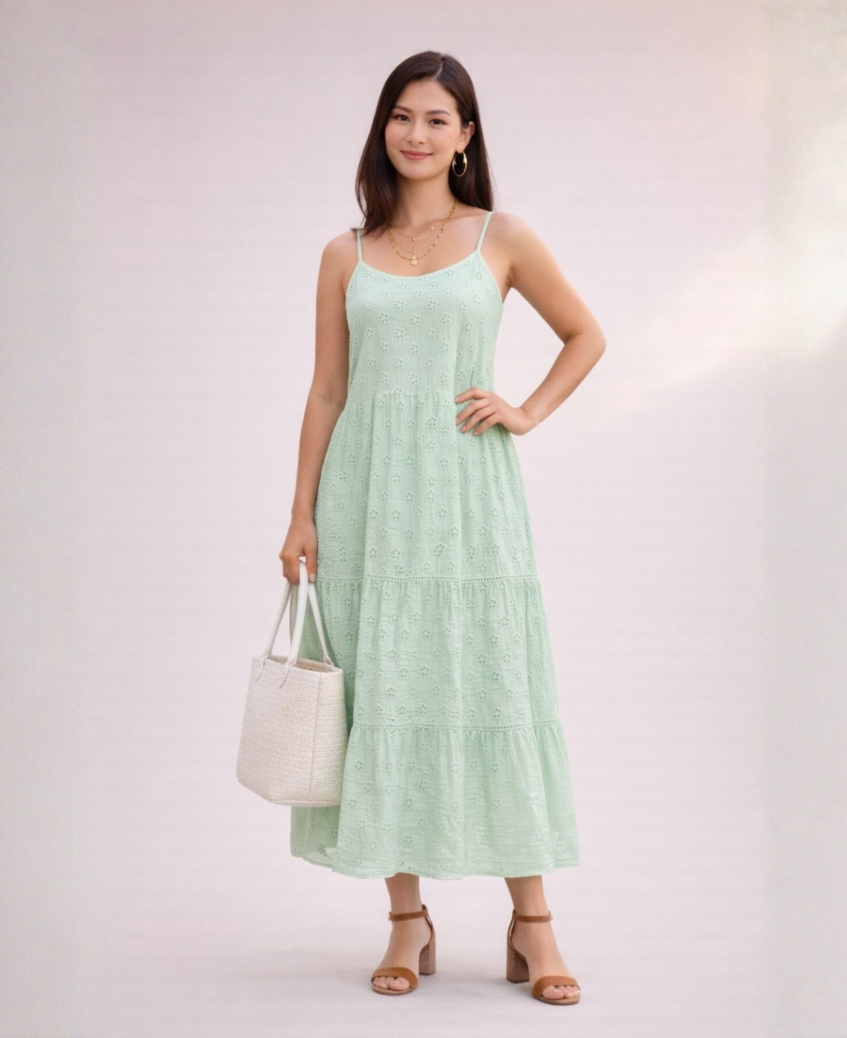 Woman wearing a mint green cotton eyelet dress with thin straps and tiered skirt against a soft neutral background