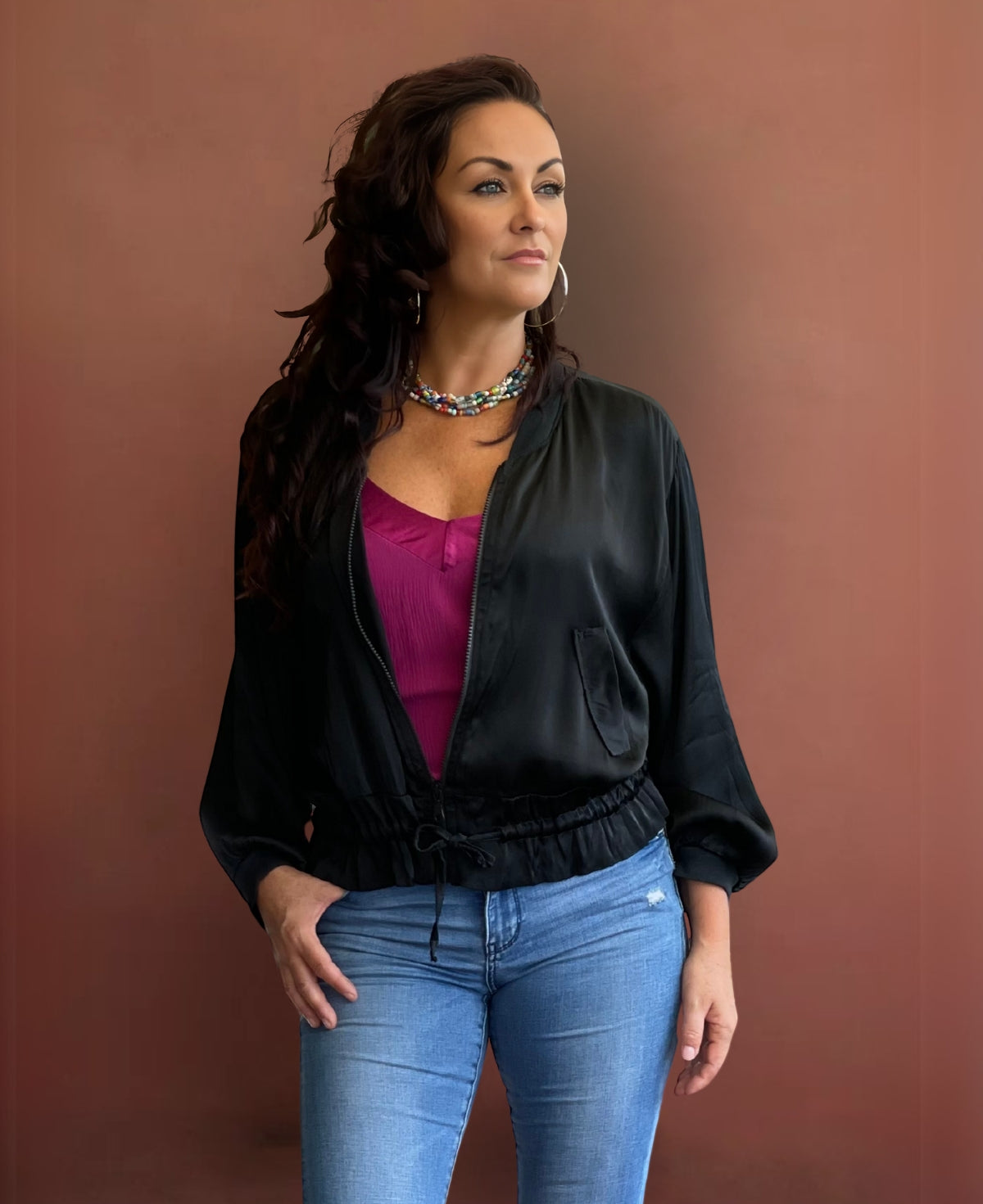 Sleek black satin bomber jacket featuring ribbed knit accents, a black gunmetal zipper, faux flap pockets, and an adjustable cinched waist for a bold yet refined look