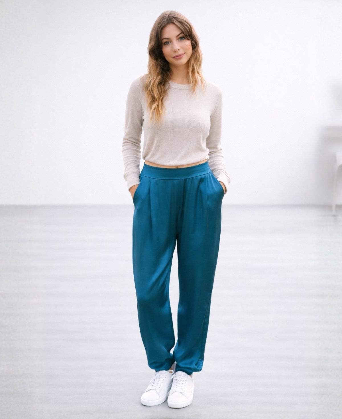 Front view of the Moulin Satin Joggers in Teal, styled casually with a knit top and sneakers, highlighting the relaxed satin fit, side pockets, and gathered ankle cuffs.