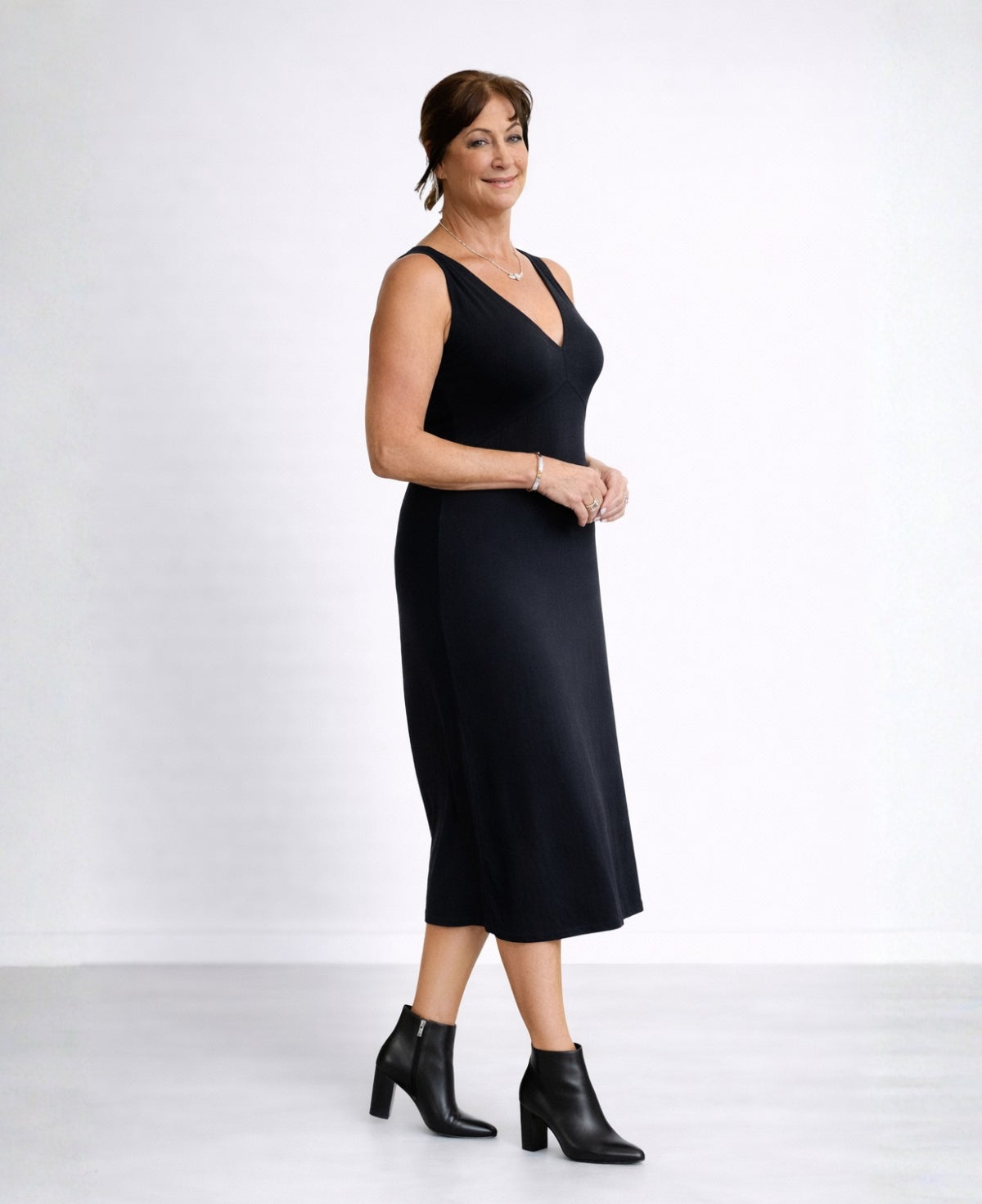 Front angled view of the Nell Knit Dress in black on mature model wearing structured black leather ankle boots in studio setting.
