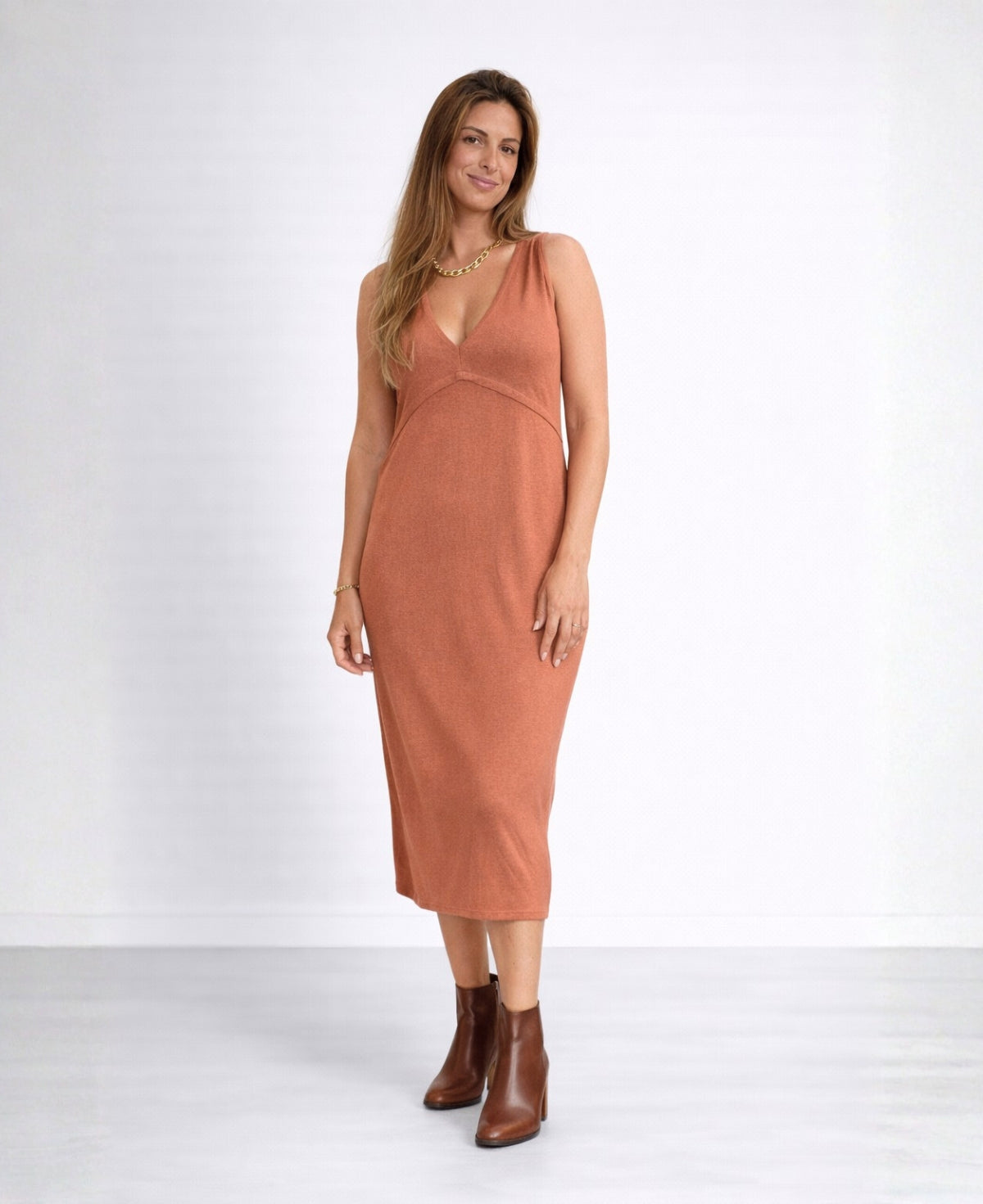 Front view of the Nell Knit Dress in warm copper colour with younger model standing relaxed in brown leather ankle boots in studio setting.