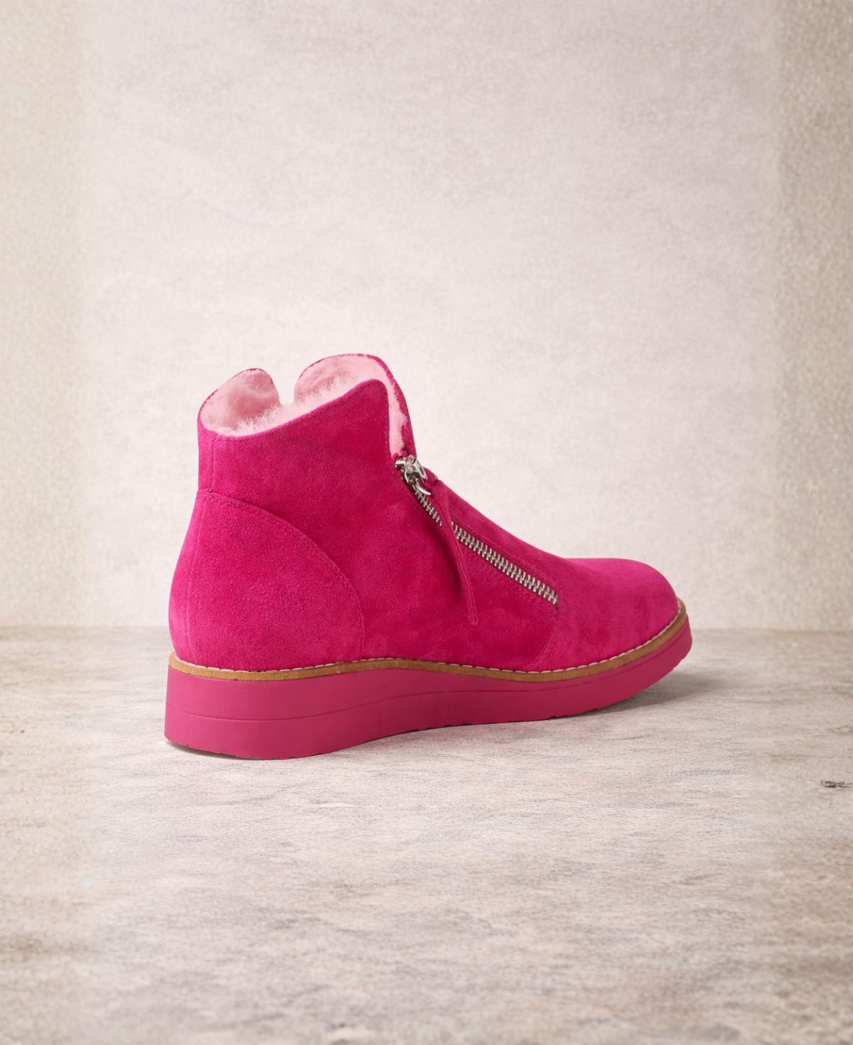 Back view of Opal fuchsia suede ankle boots showing the heel, faux fur lining and cushioned wedge sole on a soft neutral backdrop.