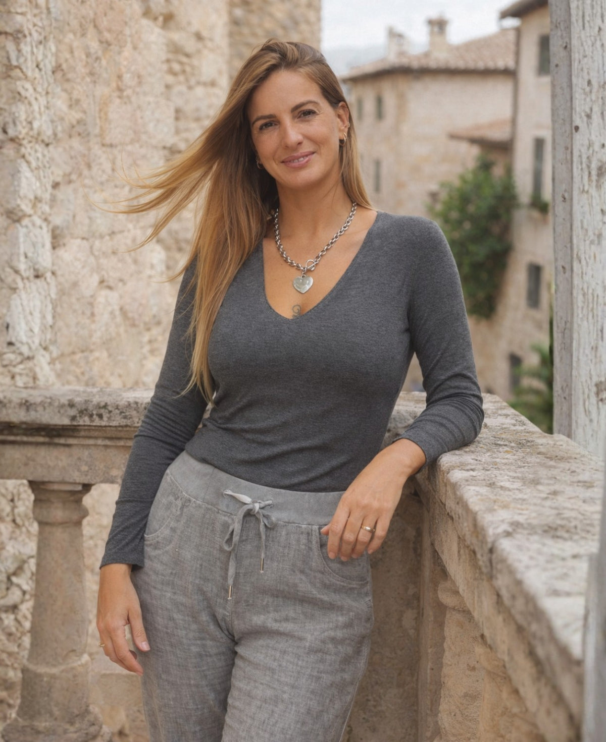 Woman wearing the Pipa Jersey V-Neck Top in grey leaning on a European stone balcony styled with relaxed linen pants.