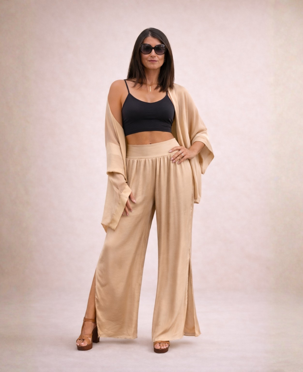 Front view of Pippa Silk Pants in Caramel silk blend, styled with matching duster off one shoulder, black cropped tank top and sunglasses, one hand on hip.
