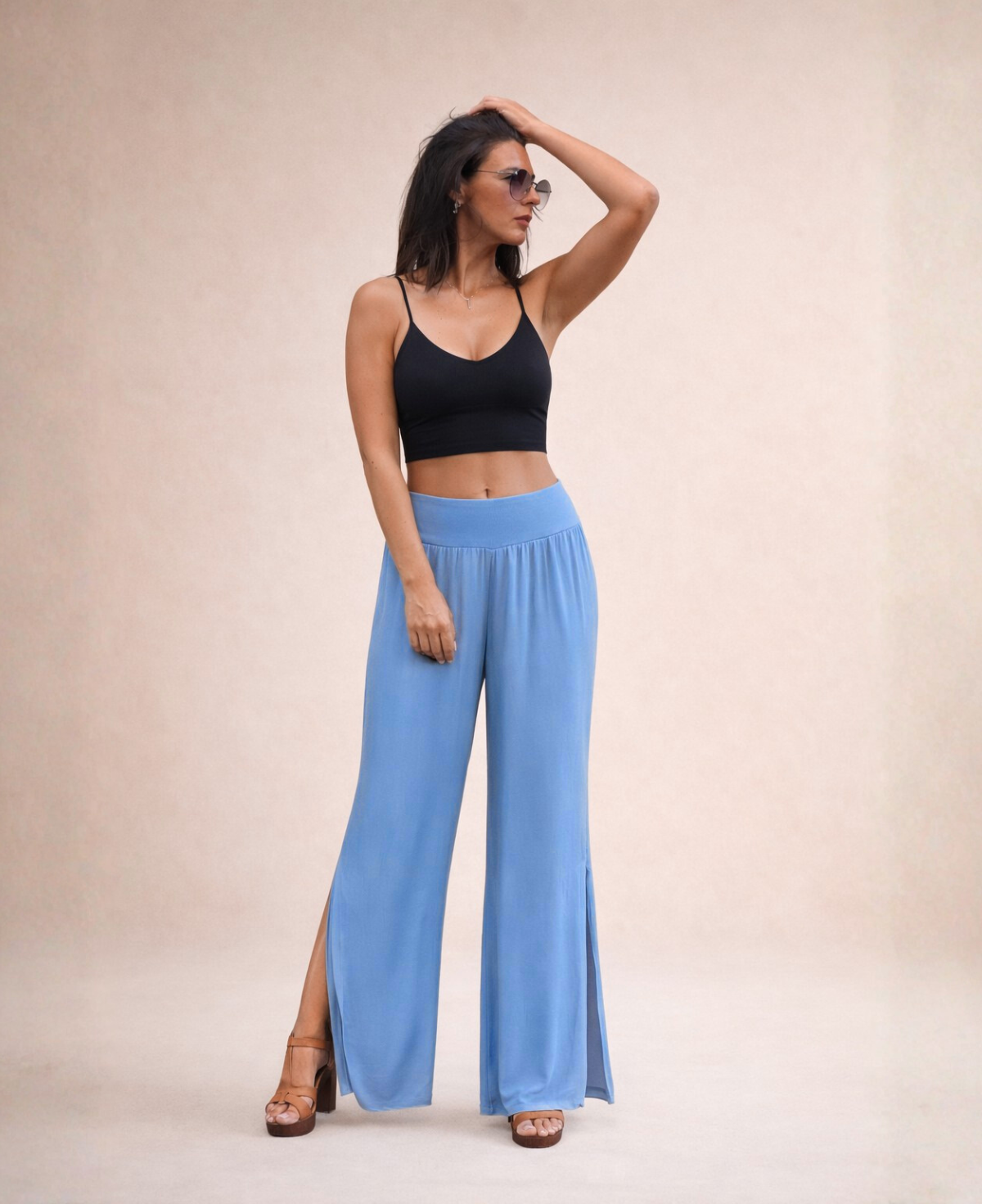 Front view of Pippa Silk Pants in Jeans blue silk blend, styled with black cropped tank top, one hand touching hair and wearing sunglasses.