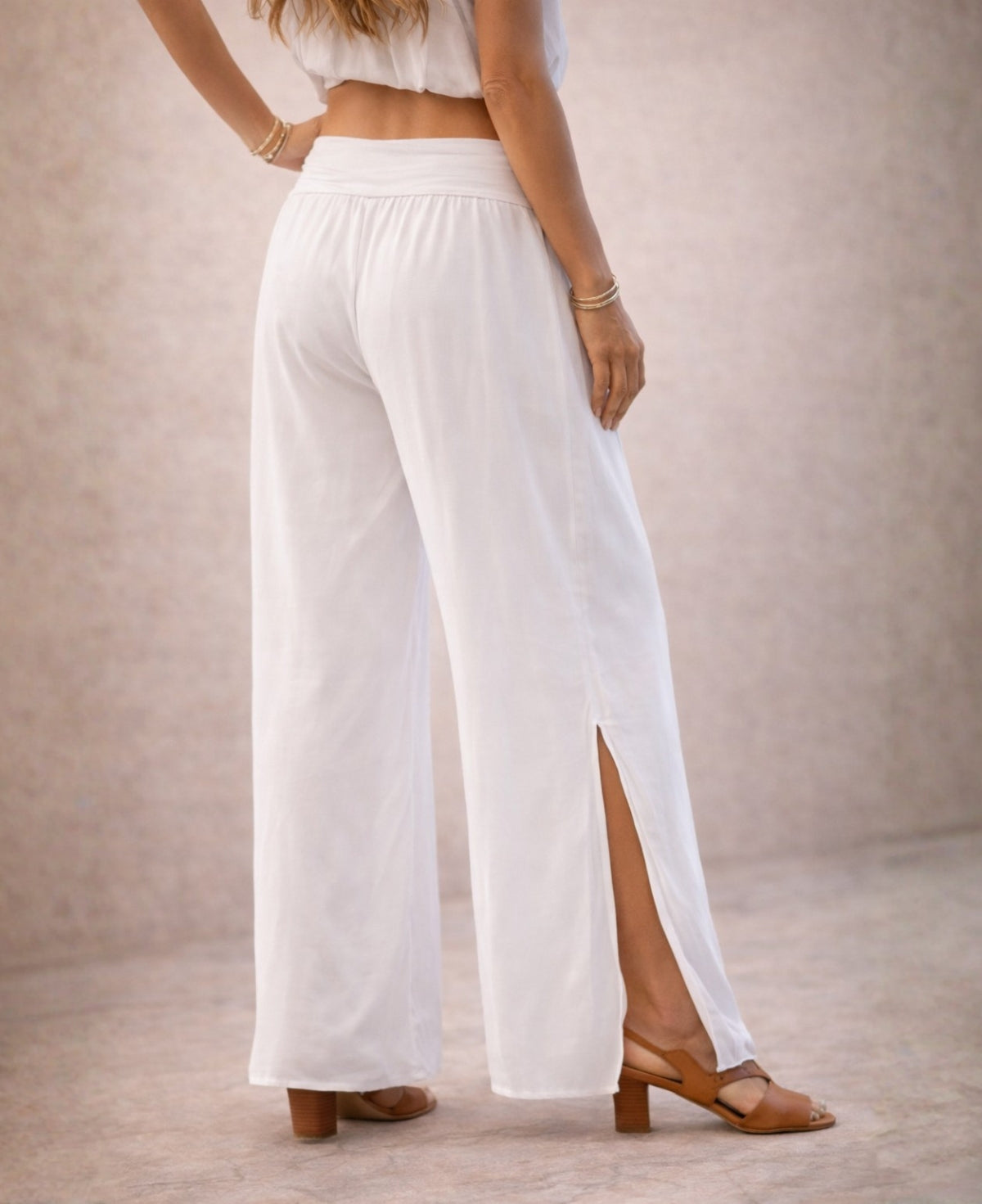 Back angled studio detail of Pippa Silk Pants in optic white silk blend, showing wide-leg volume, soft drape and knee-high side slit against a warm stone background.