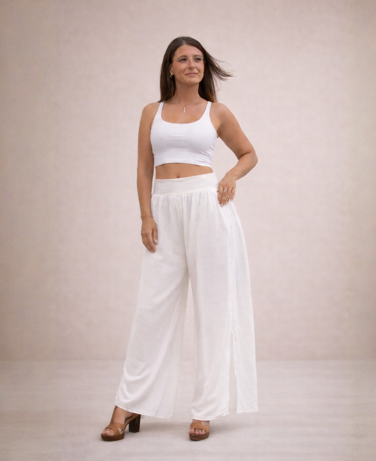 Front view of Pippa Silk Pants in White silk blend, styled with white cropped tank top, one hand on hip, head slightly turned and gentle smile in studio.
