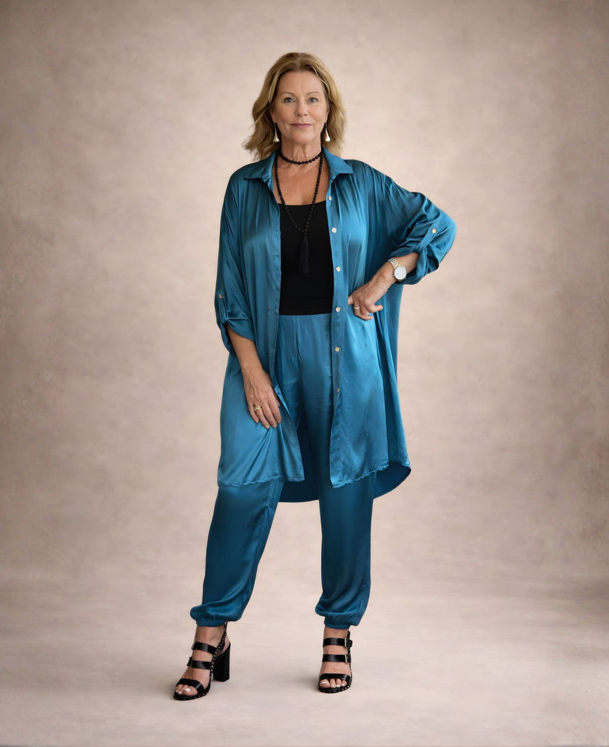 Model wearing the Porcha Satin Long Shirt-Dress in teal satin styled open as a long shirt over matching satin pants, showing the relaxed straight silhouette and high-low hemline.