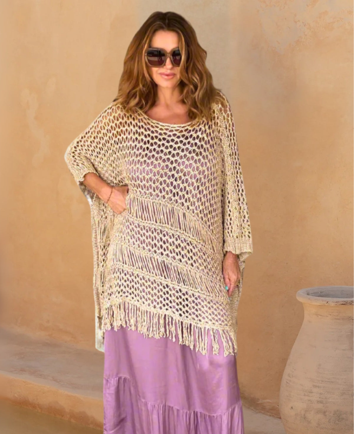 A shimmering gold poncho draped over a mauve satin dress, showcasing its lightweight knit fabric and elegant, relaxed fit for a glamorous evening look.