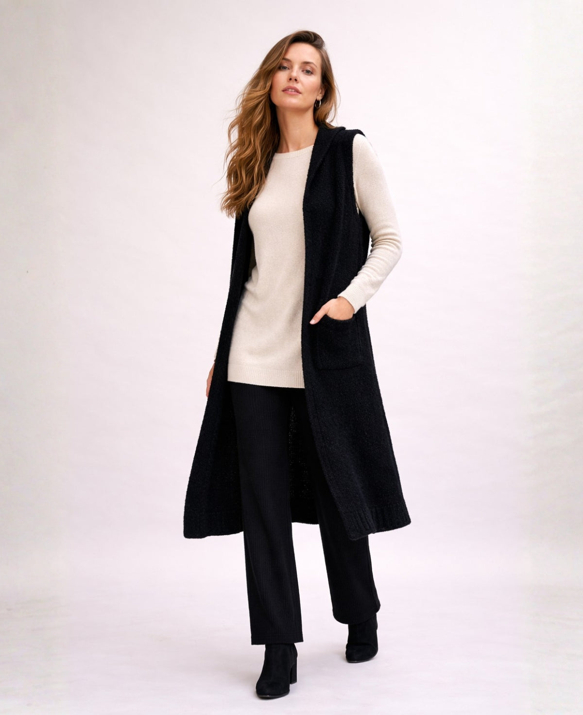Front studio image of the Rockstar Long Vest in black styled with the Le Coco Sweater in cream and Bribie black knit pants on a warm off-white background.