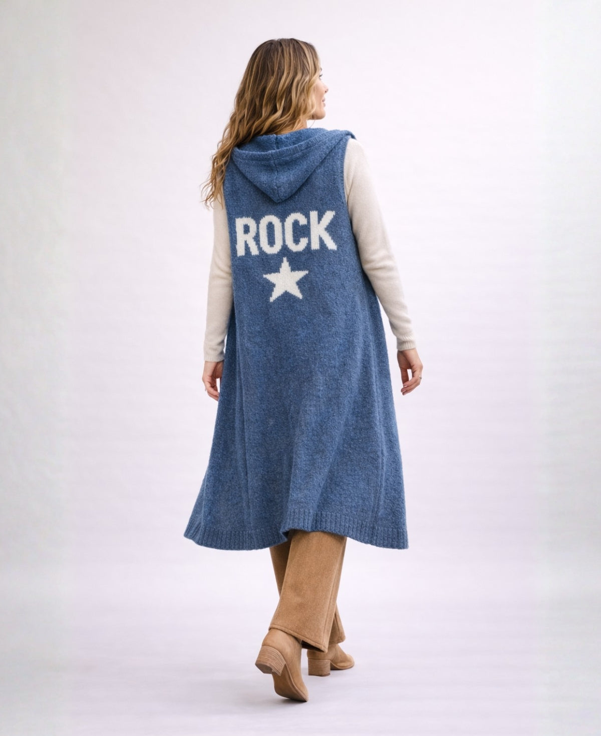 Back studio image of the Rockstar Long Vest in blue showing the white ROCK and star knitted graphic, styled with the Le Coco Sweater in cream and Bribie camel knit pants.