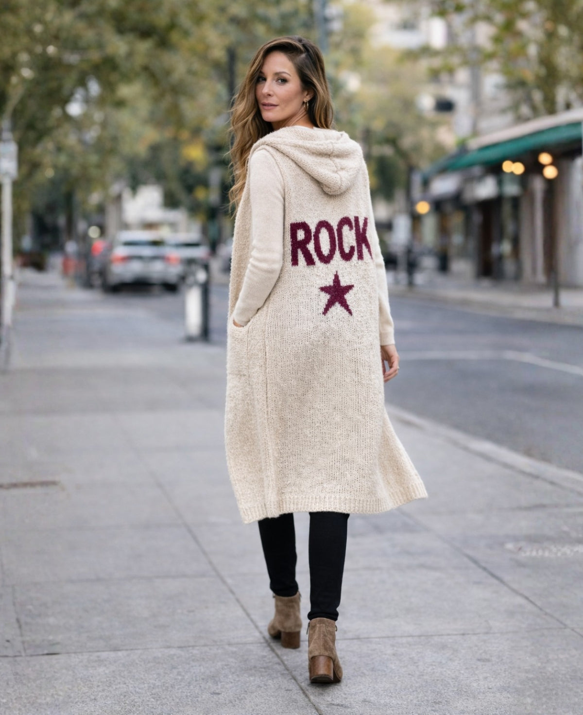 Back view of the Rockstar Long Vest in cream featuring burgundy ROCK graphic, styled with the Le Coco Sweater in cream, straight black pants and black suede ankle boots in an urban editorial setting.