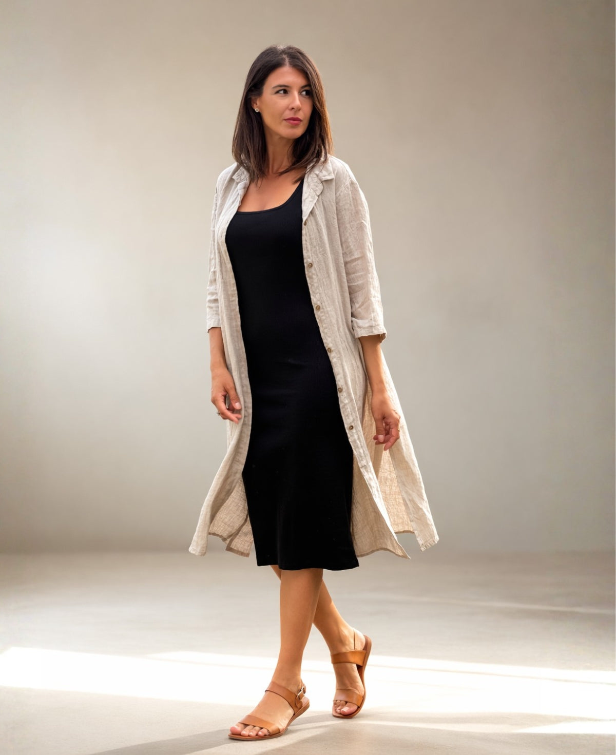 Beige Samira Linen Shirt-Dress styled open over a black jersey dress, 3/4 studio view showing drape, side seam pockets and layering versatility.
