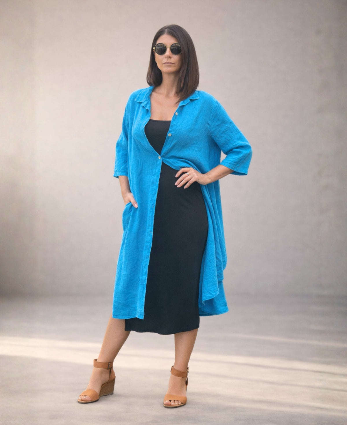 Turquoise Samira Linen Shirt-Dress worn open over a black dress, studio view with hand in side pocket highlighting fluid linen movement.