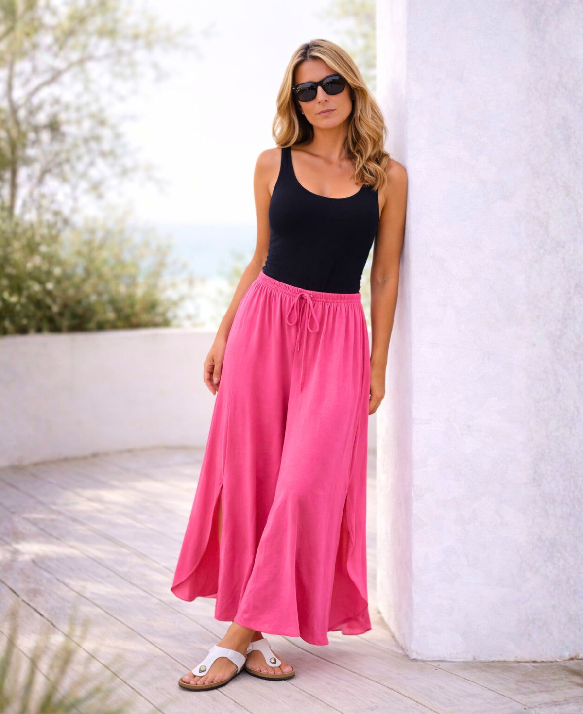 Model wearing pink Somma rayon wide leg pants leaning casually against a white column