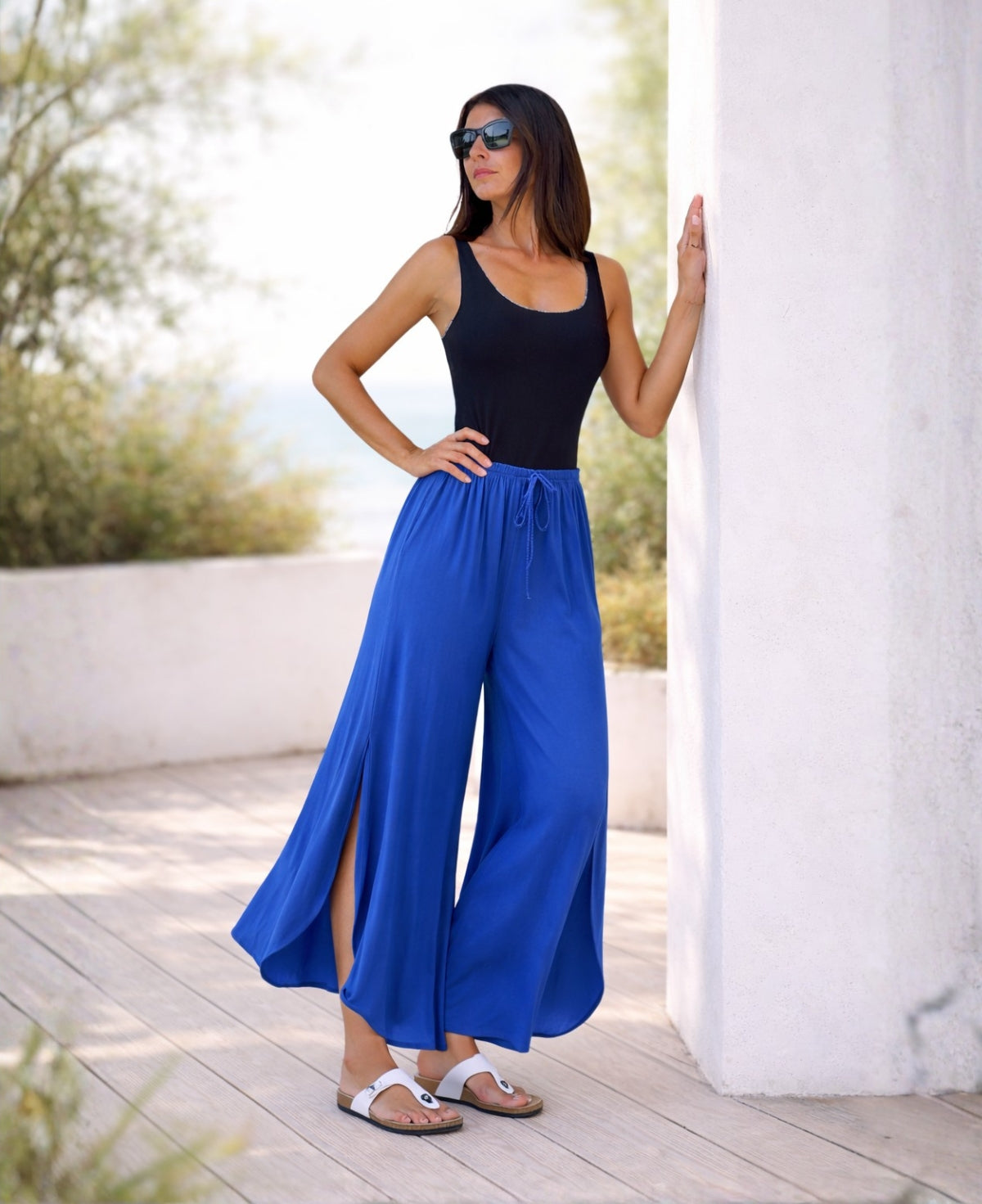 Model wearing cobalt Somma rayon wide leg pants leaning against a white column outdoors