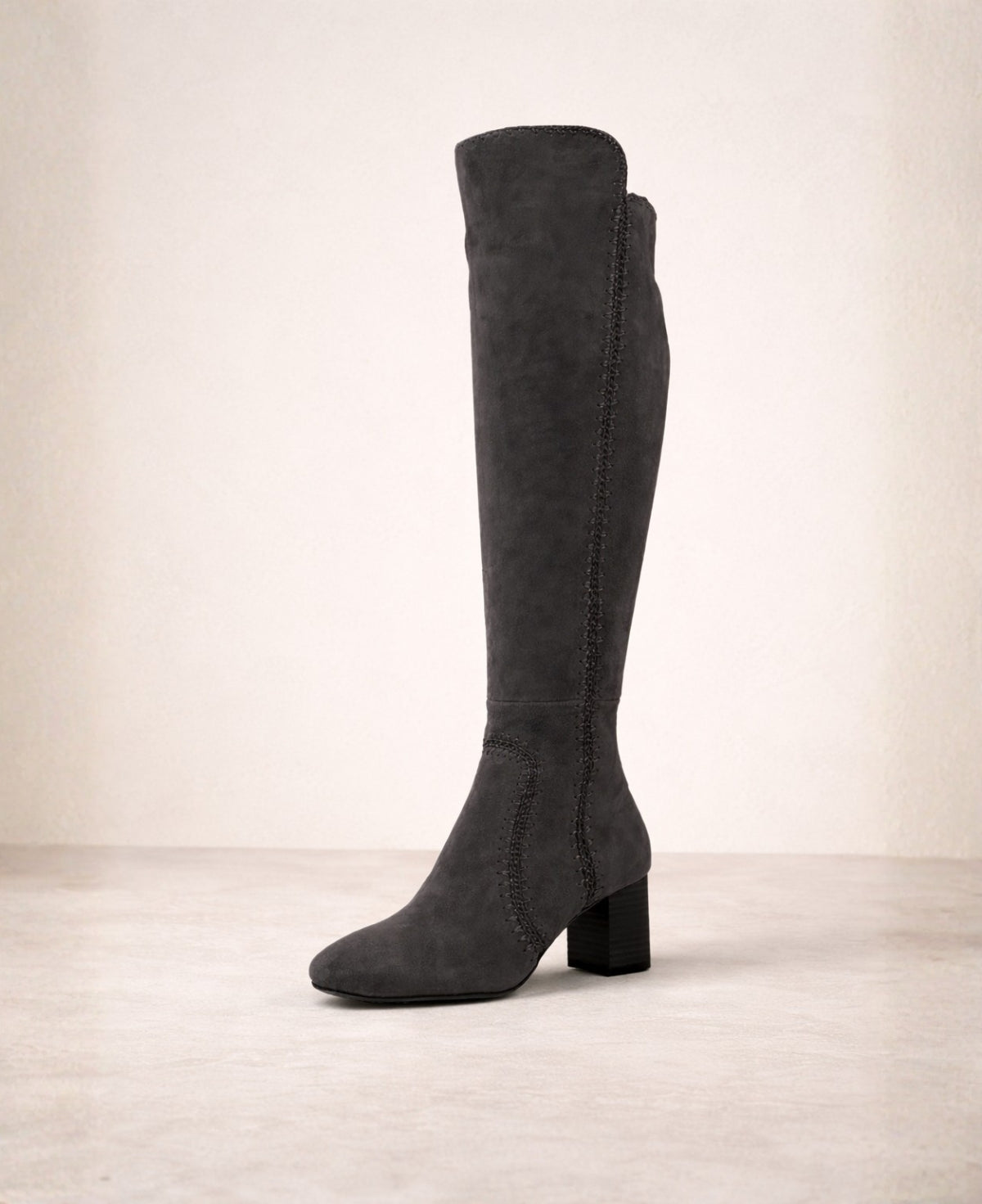 Black suede knee high boots with swept top edge, decorative stitching and mid block heel shown from the outer side