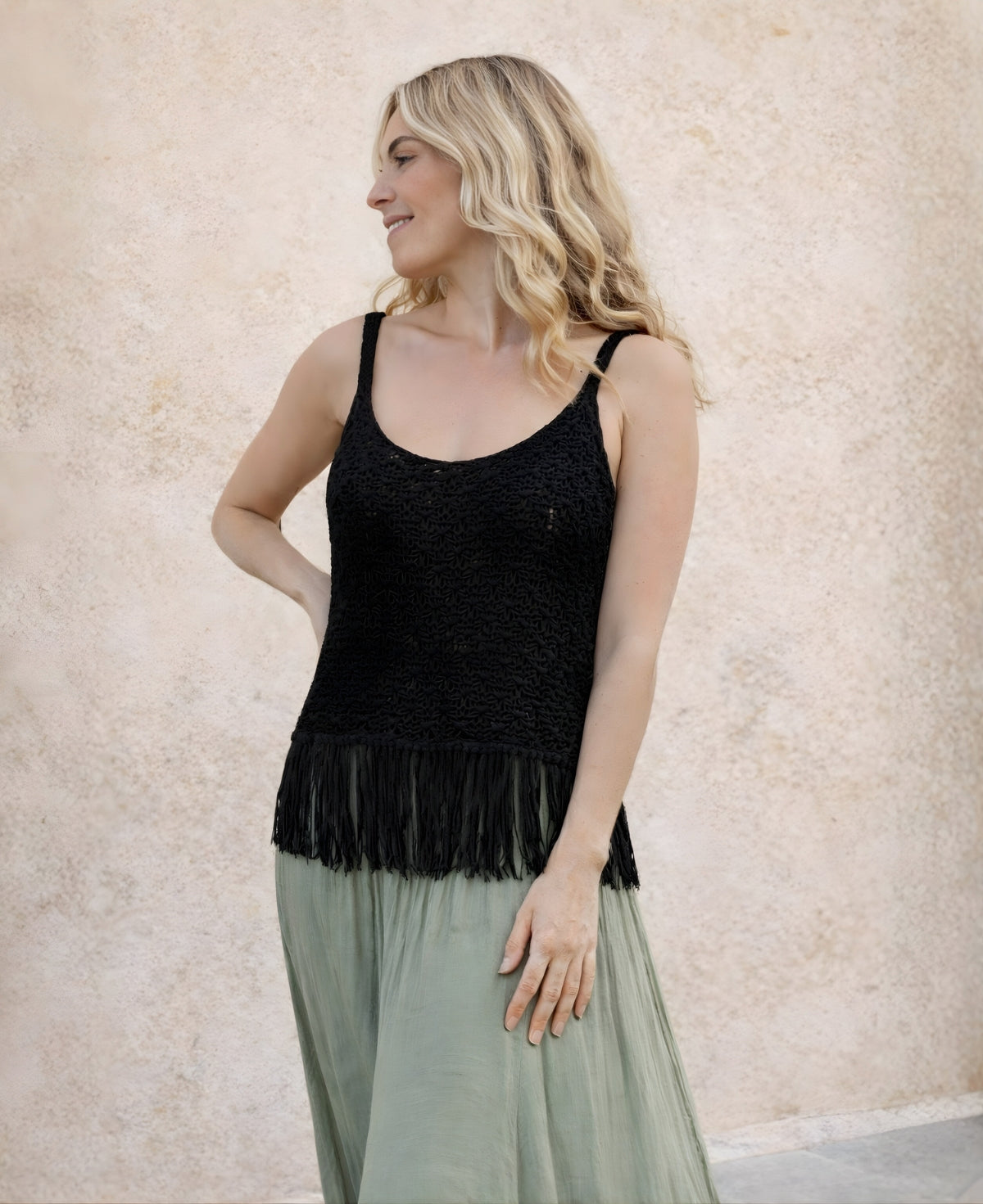 Black crochet fringe tank top worn by model against soft Mediterranean textured wall