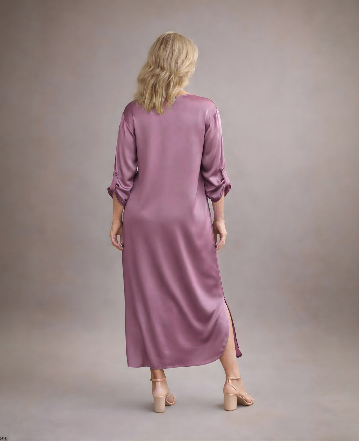 Back view of dusty pink satin Valene dress showing seamless construction, soft A-line drape and rounded side split against warm mushroom studio backdrop.