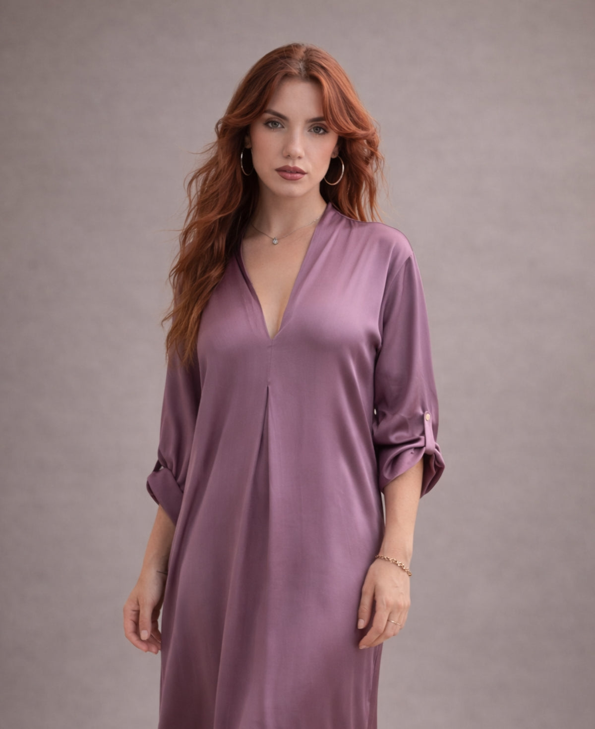 Close-up detail of dusty pink satin Valene midi dress featuring V-neckline, soft sleeve tabs and fluid drape, styled with minimal gold jewellery in warm neutral studio backdrop.