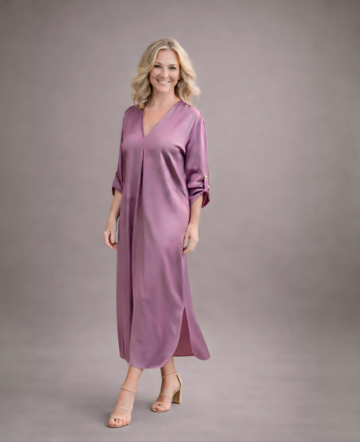 Front angled view of dusty pink satin Valene midi dress with V-neckline and fluid A-line silhouette styled with nude heels in neutral studio setting.