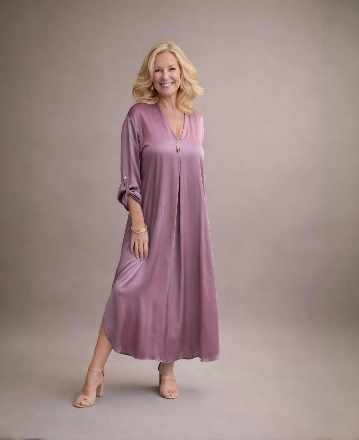Front view of dusty pink satin Valene dress featuring V-neckline, relaxed sleeves and softly rounded side split in warm neutral studio light.