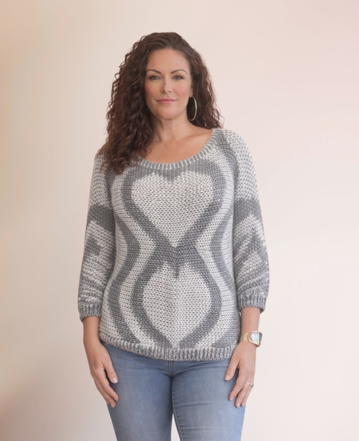 Model wearing the Valentine Wool Blend Jumper in Silver with grey heart knit pattern, styled with blue jeans against a soft neutral studio background.