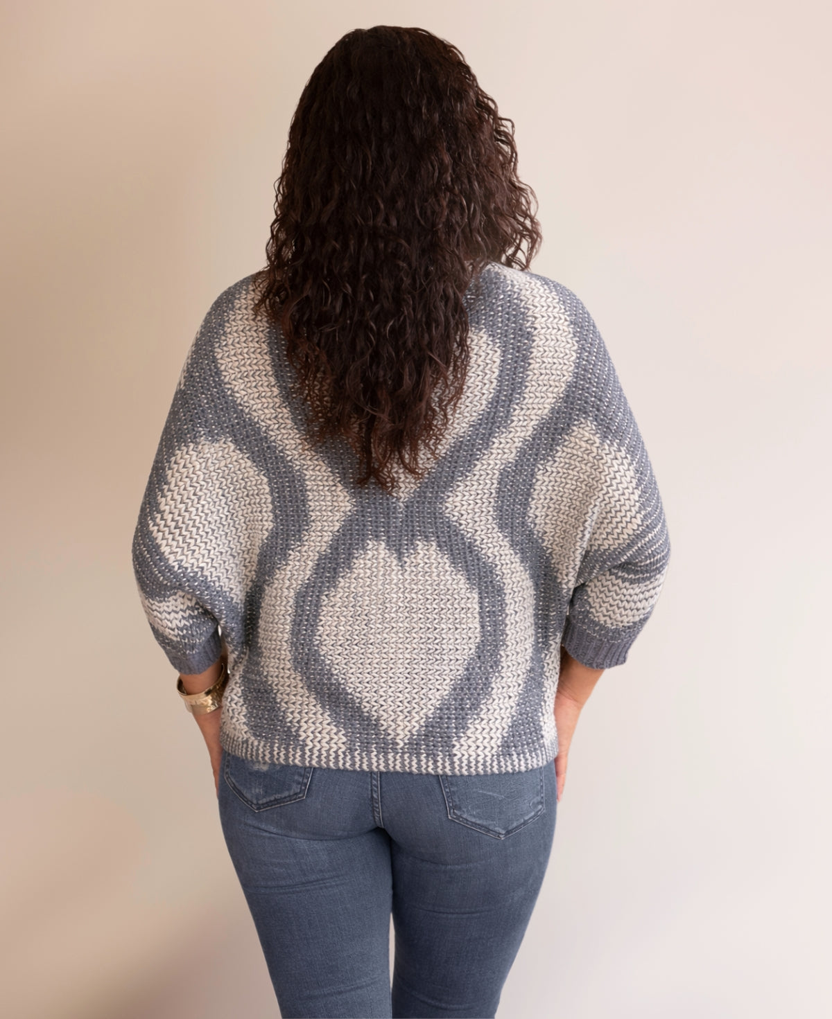 Back view of the Valentine Wool Blend Jumper in Silver grey showing the tonal heart knit pattern across the back, styled with blue jeans against a minimalist neutral studio background.