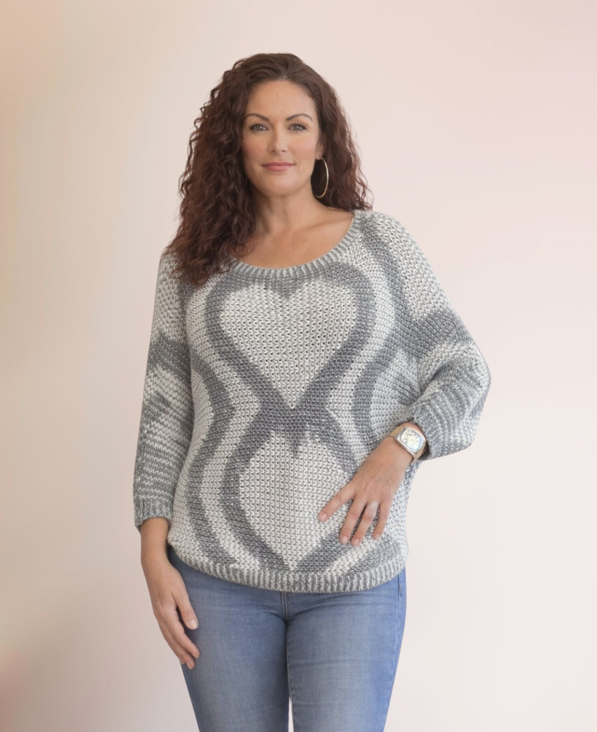 Model wearing the Valentine Wool Blend Jumper in Silver grey with tonal heart knit pattern, styled with blue jeans, shown in a confident front pose with hand on hip against a neutral studio background.
