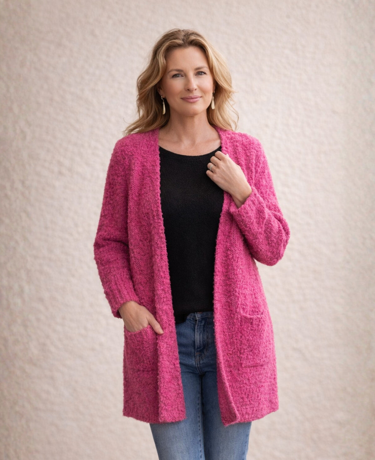 Close view of pink textured bouclé cardigan styled with black top and denim, shown against soft Mediterranean cream wall background.