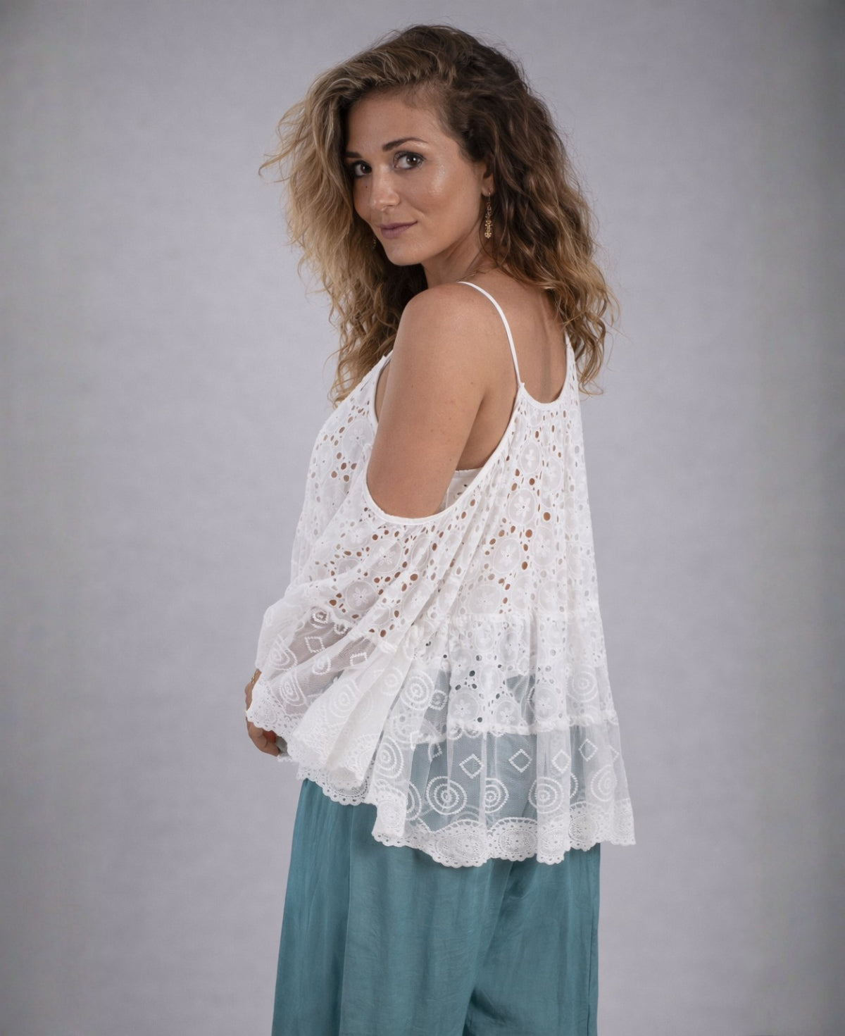 Side view of a white lace boho top with cold shoulder design and sheer embroidered sleeves, showing flowy fit and lightweight cotton fabric in a soft grey studio setting