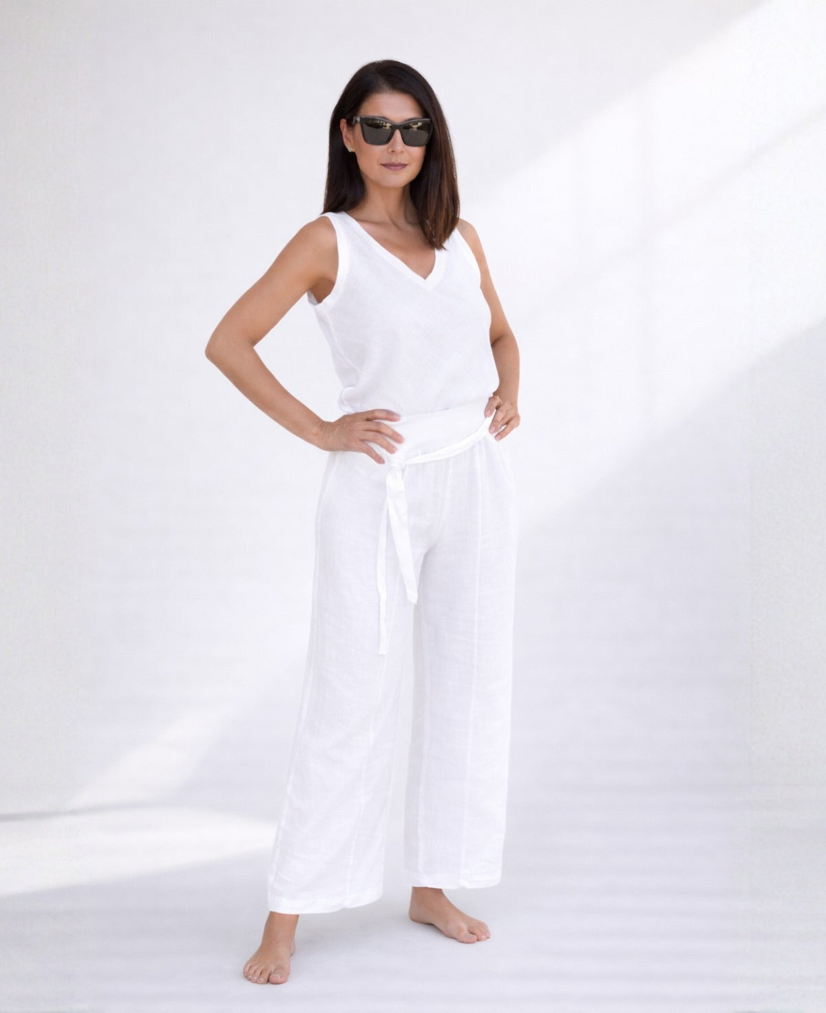 Woman wearing white linen palazzo pants with wide legs and stretch waist, front view showing optic white tone and lightweight linen fabric.