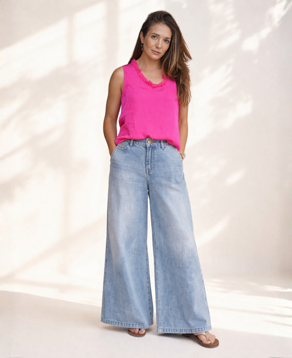 Hot pink satin sleeveless top with ruffle neckline worn front view with wide leg jeans in soft studio setting