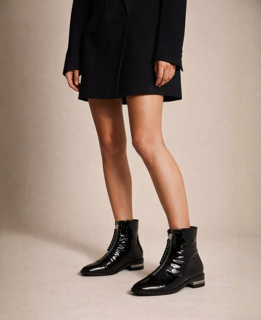 Black patent leather ankle boots worn with blazer dress, front zip detail visible
