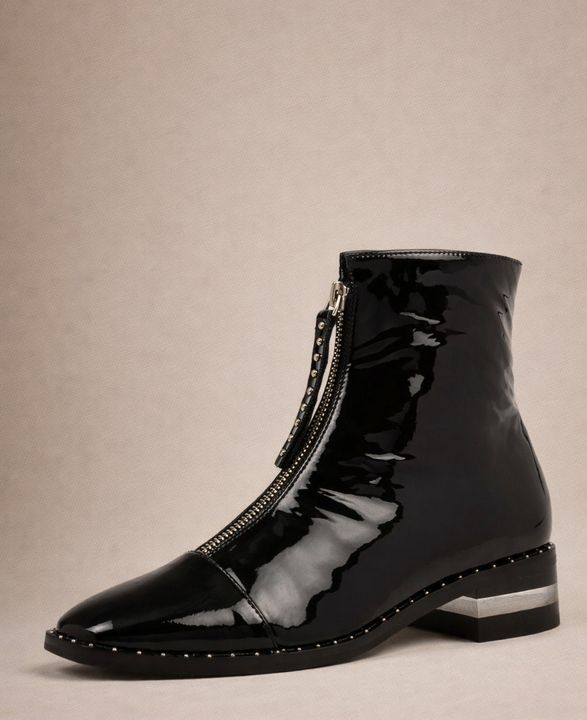 Black patent leather ankle boots in front angled studio view with front zip, low heel and stud detailing
