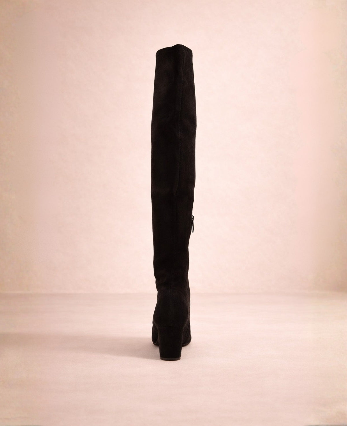 Back view of black over-the-knee boots showing the fitted shaft and block heel in a soft warm studio setting.