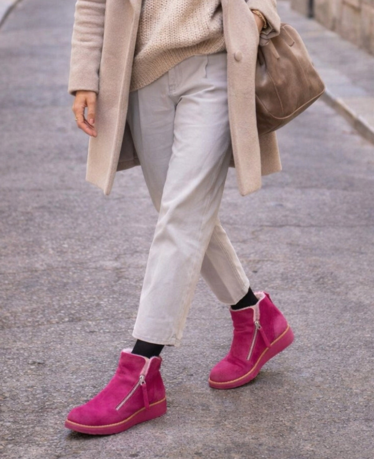Woman wearing Opal fuchsia suede ankle boots styled with neutral tones while walking through a quiet city street.