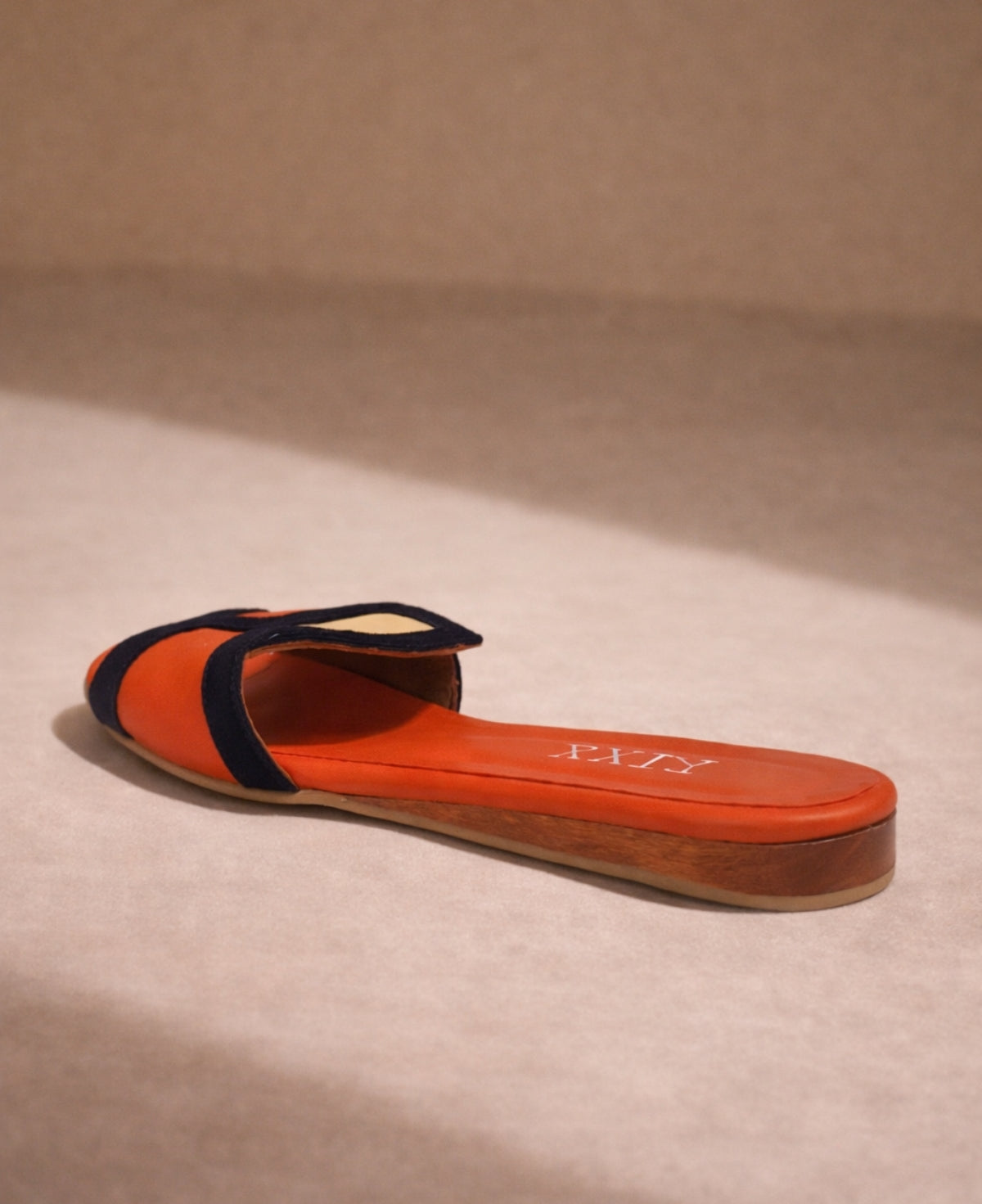 Rear angle of leather slide sandal in coral with navy detail showing heel and structure