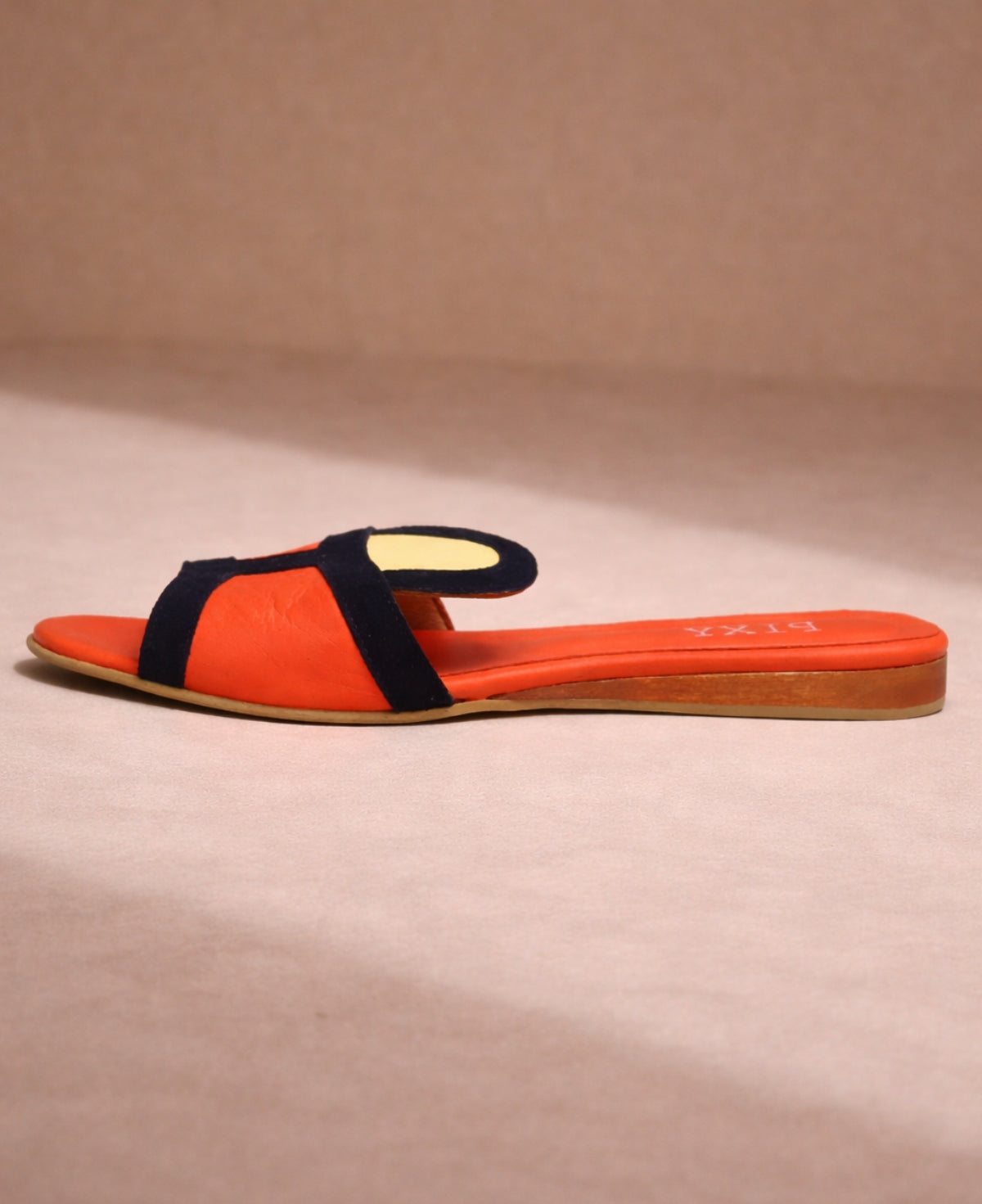 Side view of coral leather slide sandal with navy strap showing flat sole and slim profile