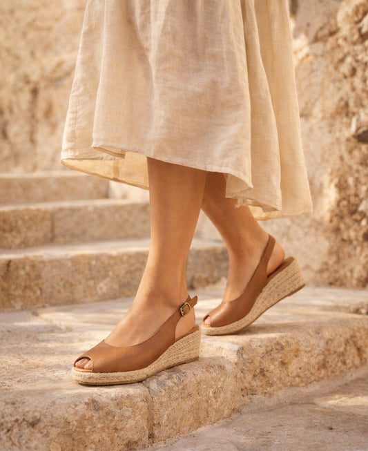 Woman wearing tan leather espadrille wedge sandals on stone steps with flowing neutral dress in warm sunlight