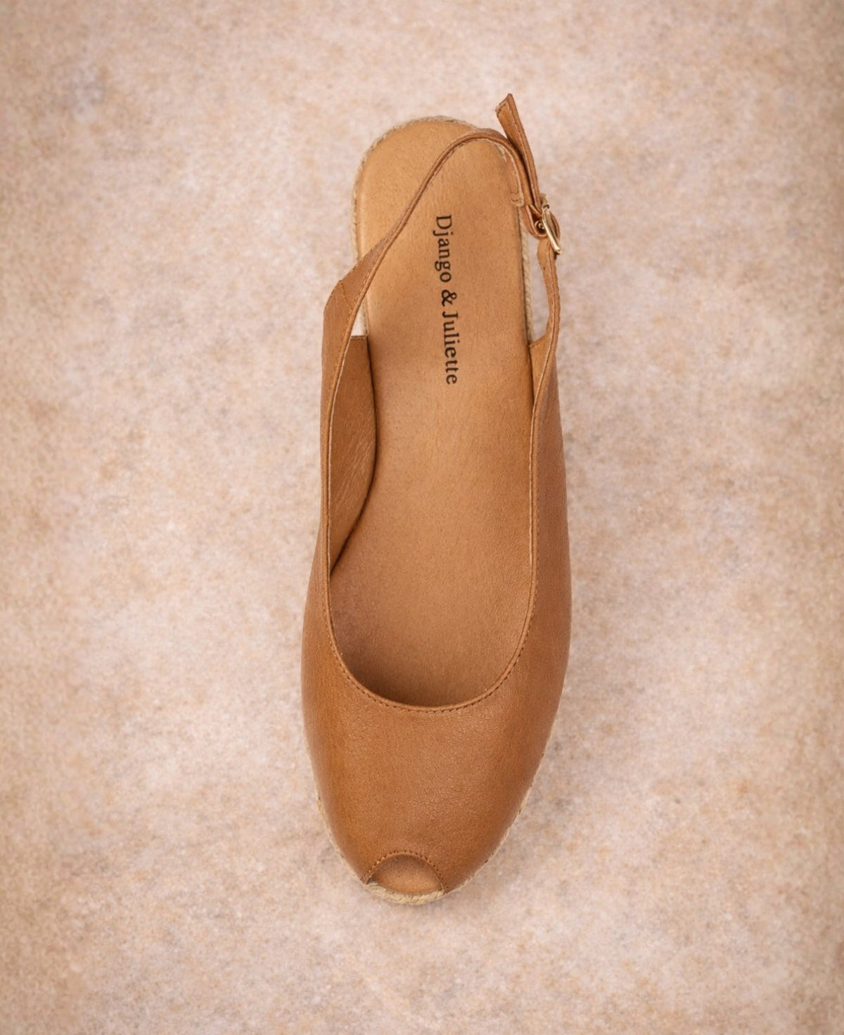 Top view of tan leather espadrille wedge sandal with peep toe and slingback strap on warm stone surface
