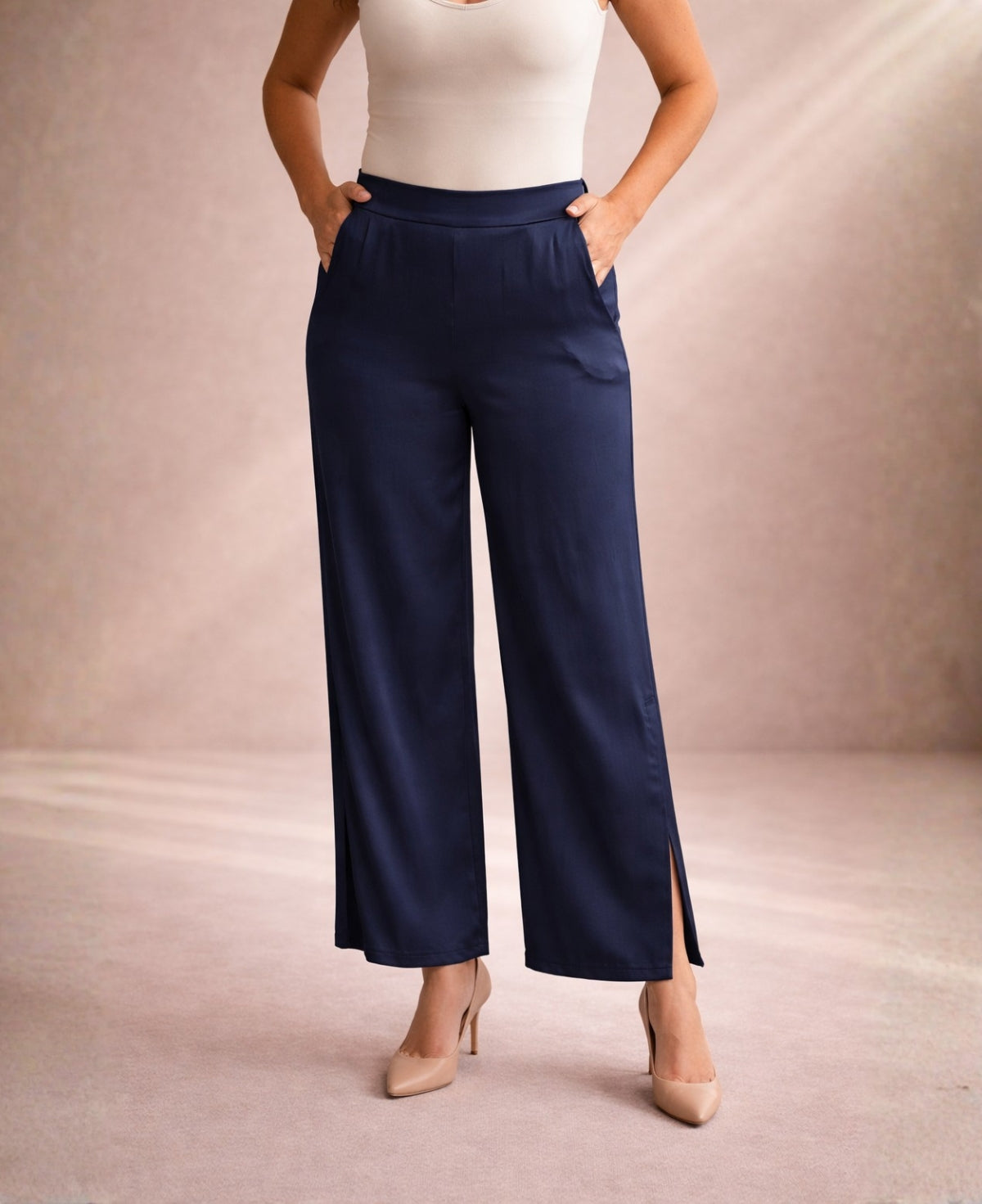 Front studio view of satin wide leg pants in navy colour with flat waistband, soft drape and calf-height side split paired with nude heels